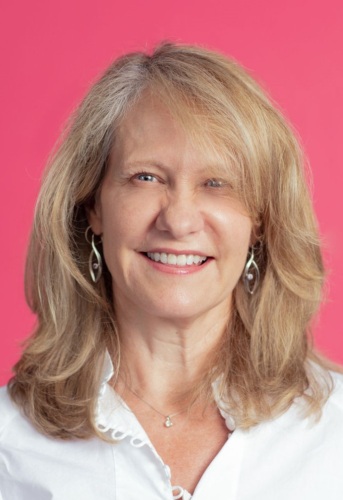 A woman in a white shirt is smiling in front of a pink background.